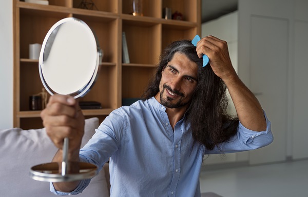 Hombre con el pelo largo peinándose el cabello delante de un espejo de mano